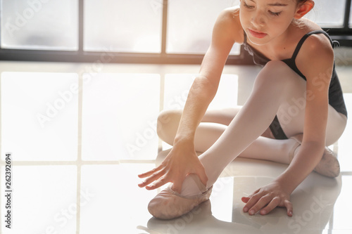 9 years old girl was sitting on the floor and tying ballet shoes for ballet class practice with the light from window background.