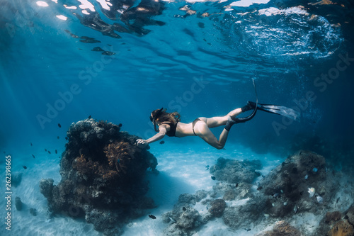 Woman freediver glides with fins and corals. Freediving underwater in blue ocean