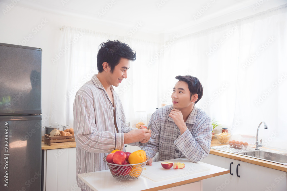 Young asian male homosexual couple eating apple for breakfast in kitchen