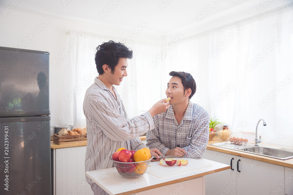 Young asian male homosexual couple eating apple for breakfast in kitchen