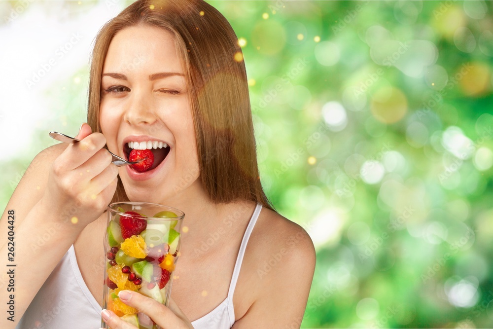 Young woman eating fruits from glass on blurred background Young woman eating fruits from glass on blurred background