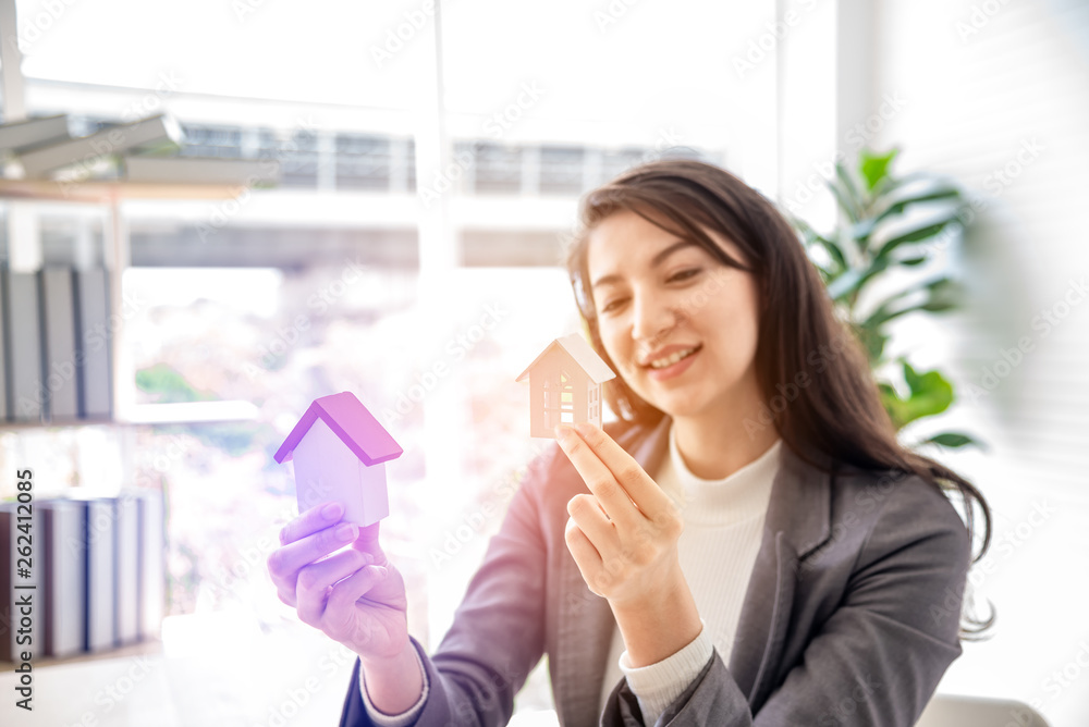 Happiness smiley young woman holding two small wooden mockup homes model in hands. Choice of Mortgage property insurance and business real estate concept. Happiness smiley young woman holding two small wooden mockup homes model in hands. Choice of Mortgage property insurance and business real estate concept.