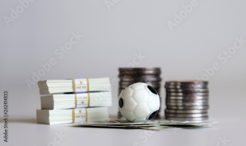 A miniature soccer ball with a pile of coins and bills.