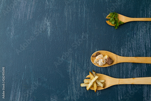 Cucharas de madera con ingredientes para preparar carne con papas y cilantro en un fondo azul desgastado con composicin minimalista y espacio para texto photo