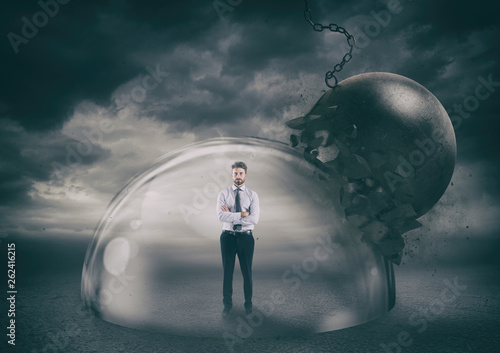 Businessman safely inside a shield dome during a storm that protects him from a wrecking ball. Protection and safety concept