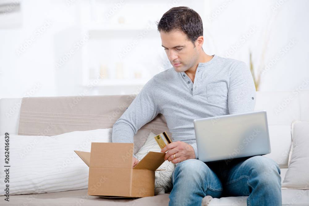 man on sofa with carton holding laptop and card man on sofa with carton holding laptop and card