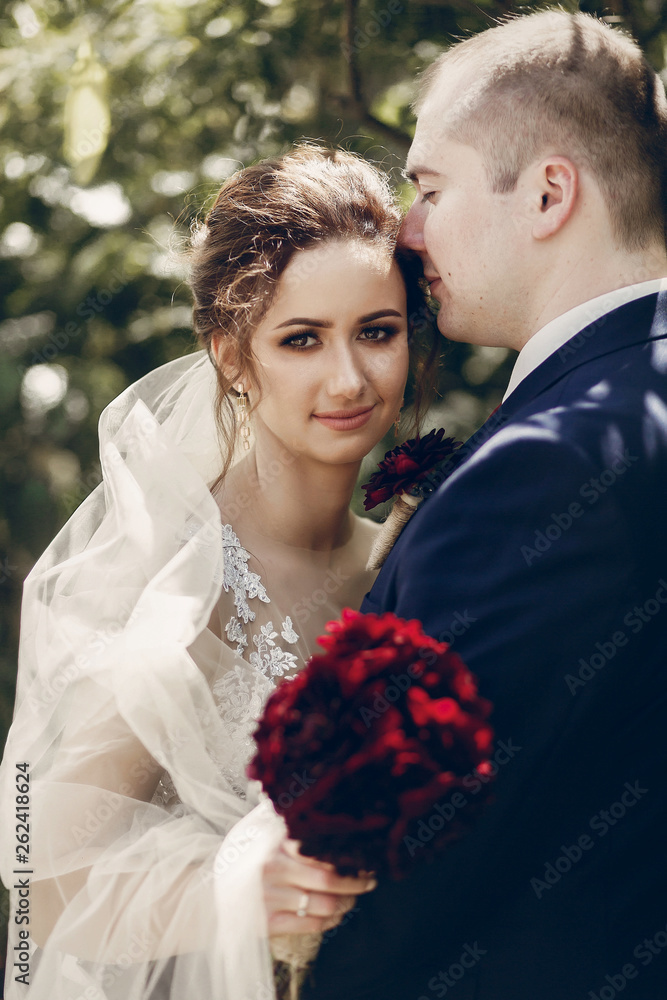 Happy newlywed couple hugging outdoors, portrait of groom kissing bride in white wedding dress in a summer park, happy moment concept Happy newlywed couple hugging outdoors, portrait of groom kissing bride in white wedding dress in a summer park, happy moment concept