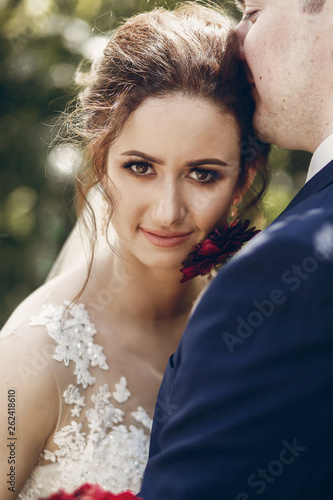 Beautiful brunette bride portrait face close-up, sensual groom kissing hugging bride, newlywed couple posing outdoors in park afrer wedding ceremony photo