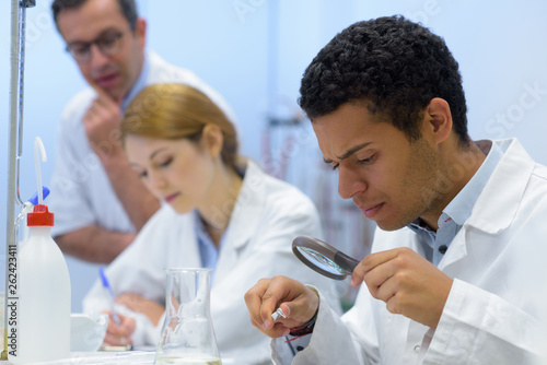 young male student using magnifying glass in science lab
