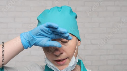 Tired female doctor removes medical mask and wipes sweat from forehead with hand. concept of a hard working day. photo