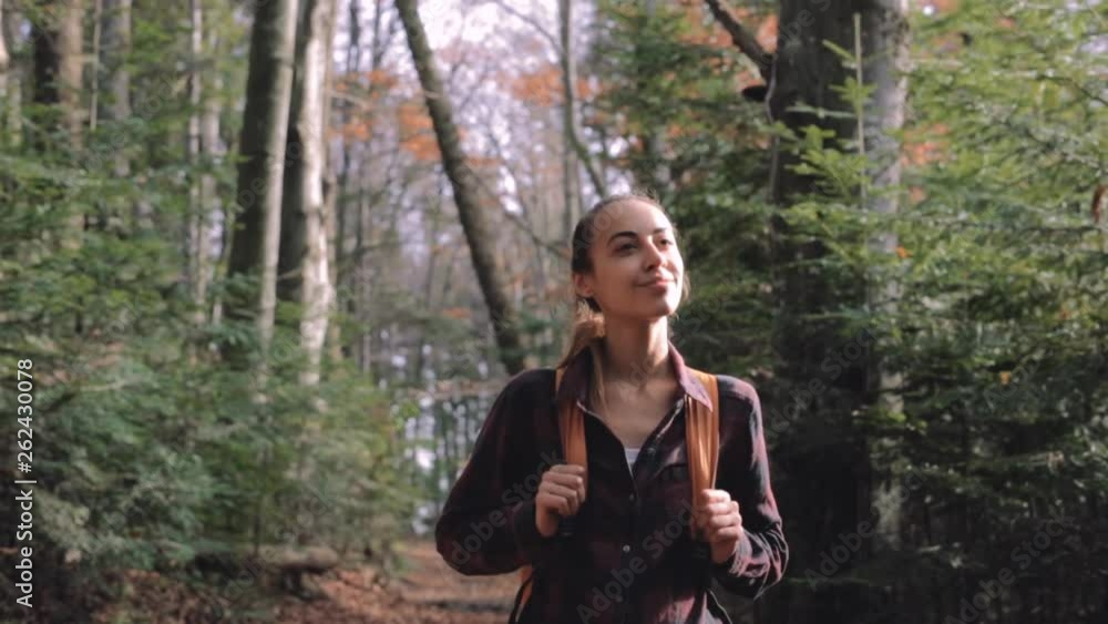 pretty woman hiker in red checkered shirt with small orange backpack is standing on the trail in pine woods with wonderful backlight from sun on background. admired woman looks around, Full HD stock pretty woman hiker in red checkered shirt with small orange backpack is standing on the trail in pine woods with wonderful backlight from sun on background. admired woman looks around, Full HD stock