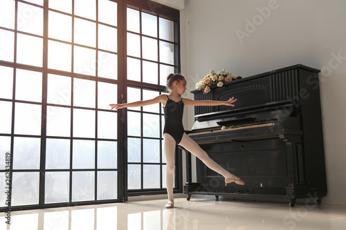 Cute ballerina 9 years old girl in black suit  dance practice in the room with old piano, kid ballet concept.