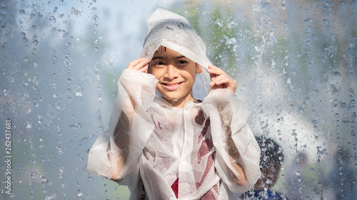 Little boy playing water drops fountain under the cloth and umbrella