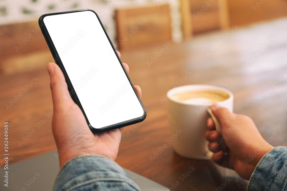 Mockup image of hands holding black mobile phone with blank desktop screen while drinking coffee Mockup image of hands holding black mobile phone with blank desktop screen while drinking coffee