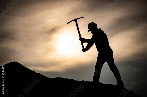 Concept Labor Day: Labor man standing holding a pickaxe with a warm sunset light