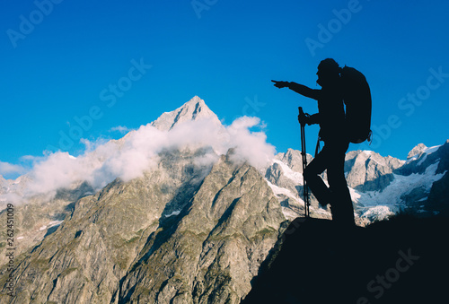 Silhouette hiking woman with backpack and trekking pole, over European Alps on the background.