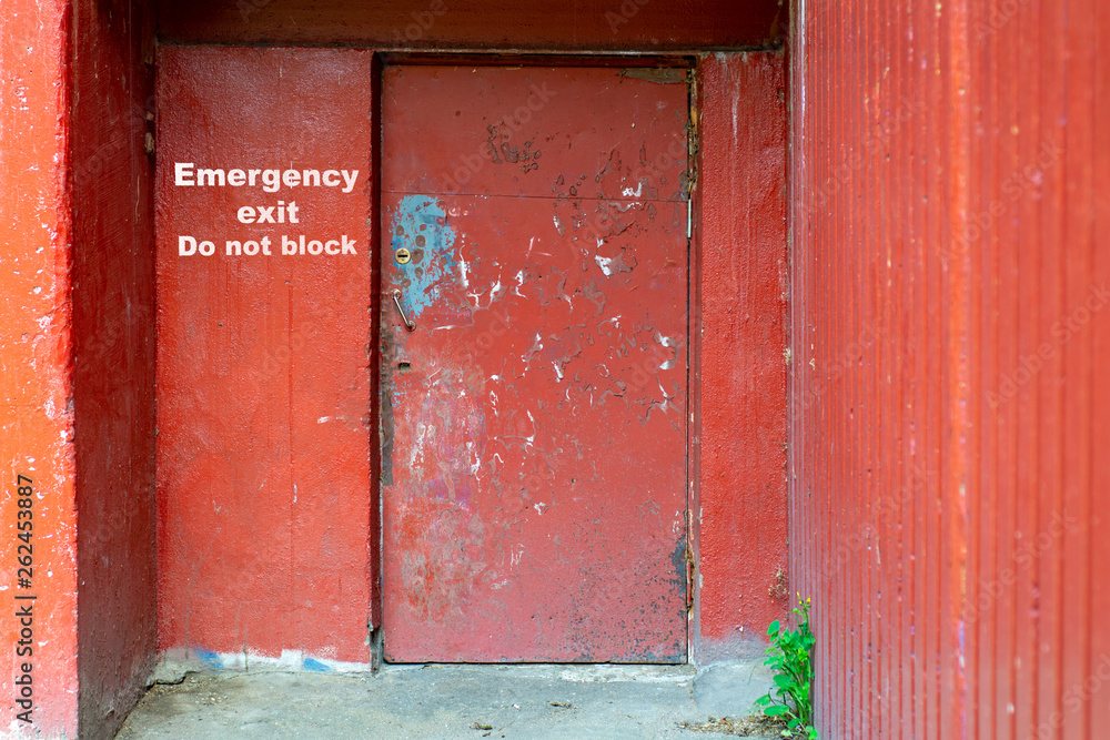 Old poor red door of an East European apartment building with inscription EMERGENCY EXIT DO NOT BLOCK Old poor red door of an East European apartment building with inscription EMERGENCY EXIT DO NOT BLOCK