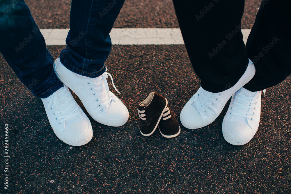 cropped male and female legs wearing white sneakers between them are sneakers for their unborn child. Family concept, baby waiting