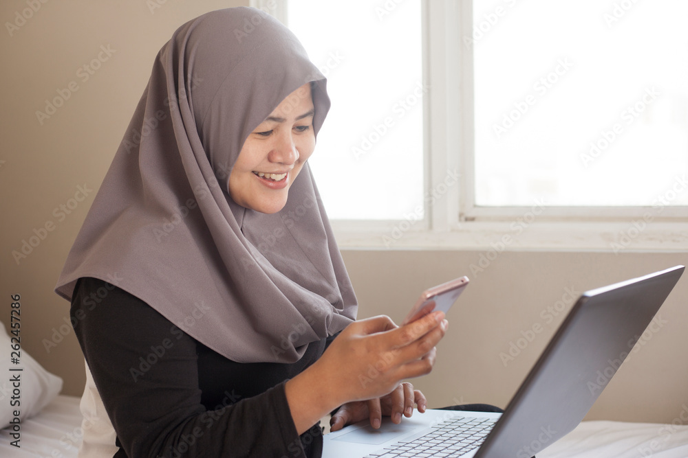 Happy Muslim Woman Working with Laptop and Smart Phone in Her Bedroom Happy Muslim Woman Working with Laptop and Smart Phone in Her Bedroom
