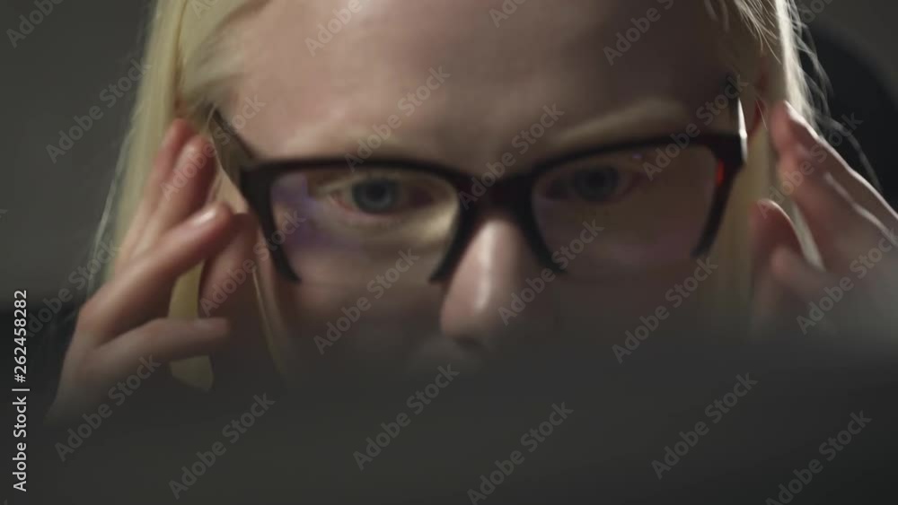 Young manager girl puts on glasses, working at computer in office, closeup of albino girl eyes, reflections on the glasses, looking at screen of computer. Young manager girl puts on glasses, working at computer in office, closeup of albino girl eyes, reflections on the glasses, looking at screen of computer.