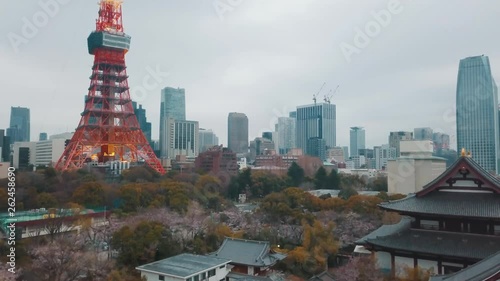 Drone panning down towards the Buddhist Zojoji Temple complex looking over the Tokyo city skyline towards the famous Tokyo Tower on an overcast hazy day with cherry blossoms blooming