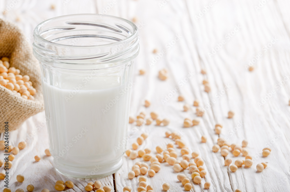 Non-dairy alternative Soy milk or yogurt in mason jar on white wooden table with soybeans in hemp sack Non-dairy alternative Soy milk or yogurt in mason jar on white wooden table with soybeans in hemp sack