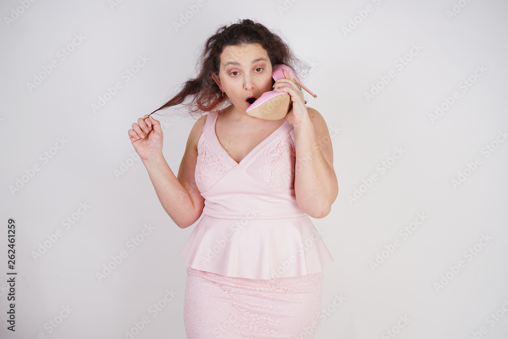 emotional plump woman in pink dress talking and gossips on the Shoe like on the phone on a white Studio background emotional plump woman in pink dress talking and gossips on the Shoe like on the phone on a white Studio background