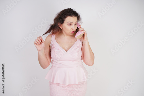emotional plump woman in pink dress talking and gossips on the Shoe like on the phone on a white Studio background