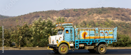 A blue truck on Indian road on a sunny morning, decorated with elaborated doodles on sides on the truck 