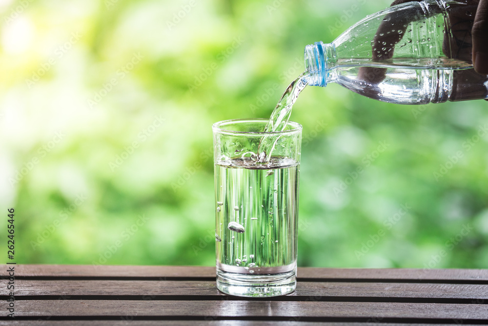 Drink water pouring into glass on wooden table over sunlight with natural lighting and background Drink water pouring into glass on wooden table over sunlight with natural lighting and background