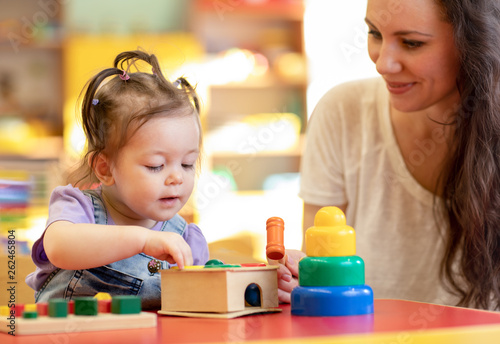 Nursery kid playing developmental toys with mother or teacher