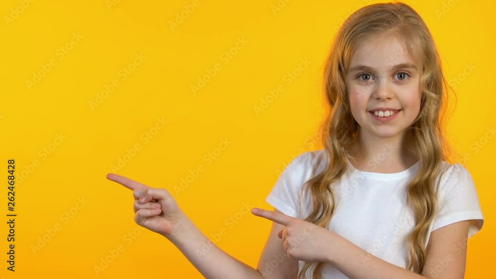 Smiling girl pointing fingers at empty space on yellow background, template Smiling girl pointing fingers at empty space on yellow background, template