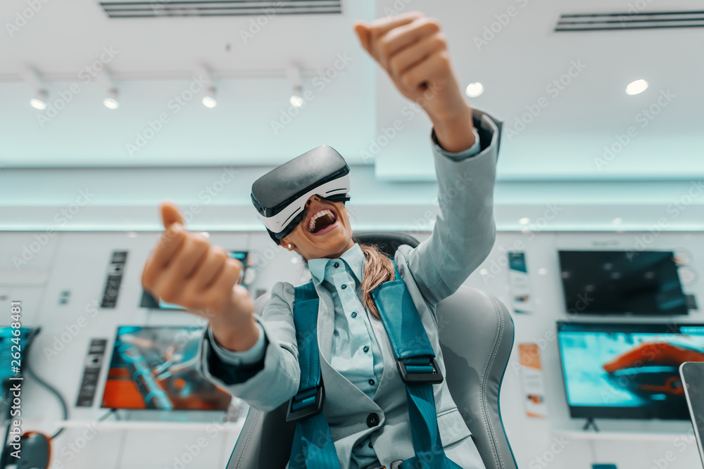 Smiling Caucasian woman in formal wear trying out virtual reality technology while sitting in the chair in tech store. Smiling Caucasian woman in formal wear trying out virtual reality technology while sitting in the chair in tech store.