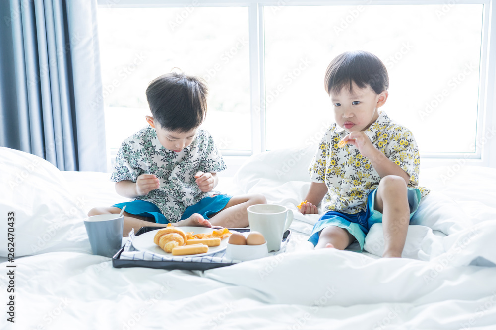 Brothers are sharing breakfast on the bed in the morning.