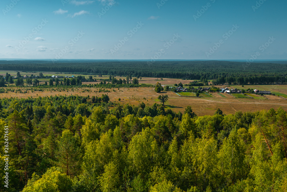 Panoramic high angle view of the plain, the village and the woods from hill top.