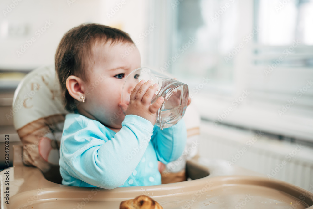 Cute little girl sitting in baby chair and drinking water Cute little girl sitting in baby chair and drinking water