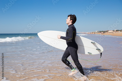 Positive man carrying surfboard and running into sea water