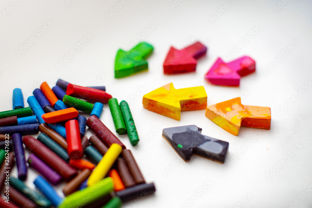 made homemade wax pencils from the wreckage of old crayons by melting them in the oven at high temperature in silicone form. crayons in the form of arrows lie on paper, hand child made homemade wax pencils from the wreckage of old crayons by melting them in the oven at high temperature in silicone form. crayons in the form of arrows lie on paper, hand child