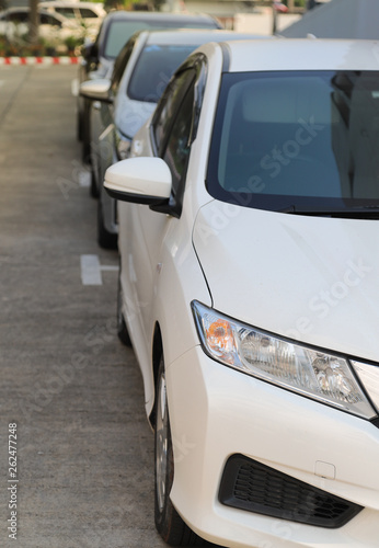 Closeup of front side of white car parking in parking area beside the street. Vertical view. © Amphon
