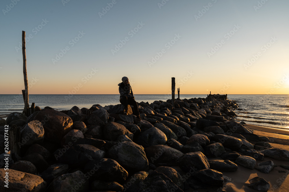 Woman enjoying a cold Spring sunset at a boulder beach near the Baltic Sea