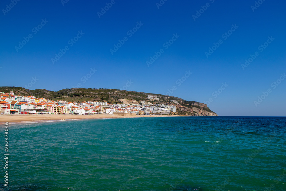 soft waves with white foam in the foreground, in the background the village of Sesimbra