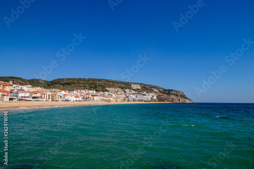 soft waves with white foam in the foreground, in the background the village of Sesimbra