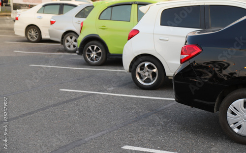 Closeup of rear, back side of black car with other cars parking in outdoor parking lot.