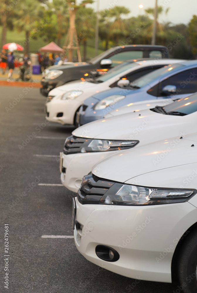 Closeup of front side of white car and other cars parking in outdoor parking area in twilight evening. Vertical view.