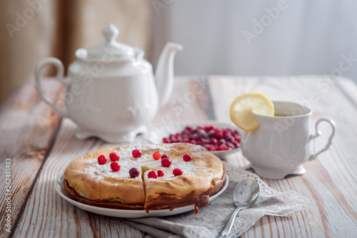 Cheesecake with cranberries and sugar, green tea and lemon on wooden table