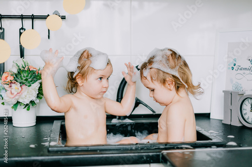 two twin girls bathing in the kitchen bathroom. play, wash their heads, laugh with each other