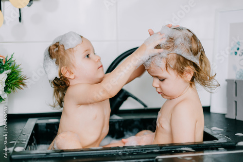 two twin girls bathing in the kitchen bathroom. play, wash their heads, laugh with each other