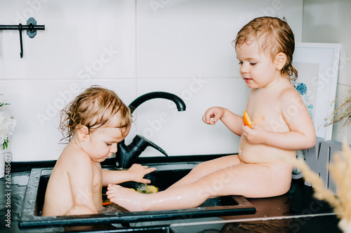 two twin girls bathing in the kitchen bathroom. play, wash their heads, laugh with each other