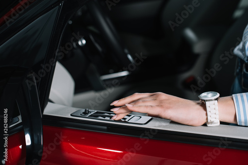 cropped view of young woman pushing button on car door in red automobile