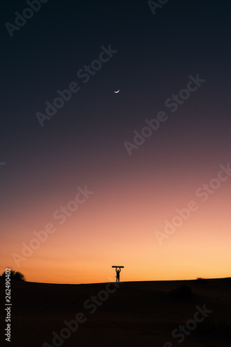 Silhouette of a man with snowboard in the Sahara desert, sunset and moon